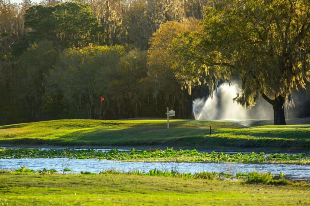 Course greens with sprinklers on in the background and lake in the foreground 