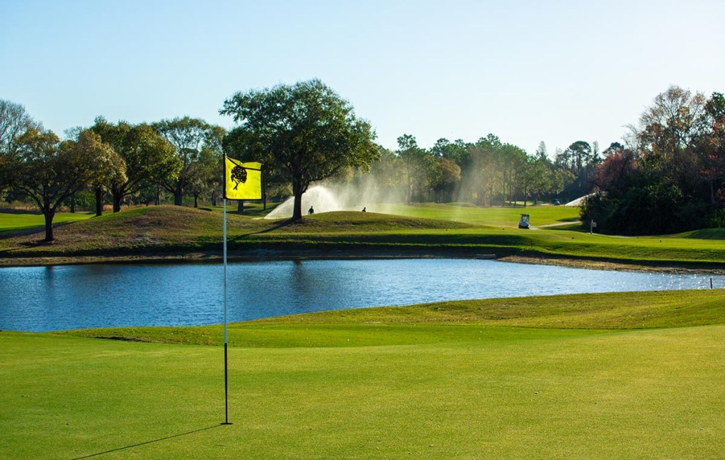 Course greens with a blue pond behind a yellow flagpole