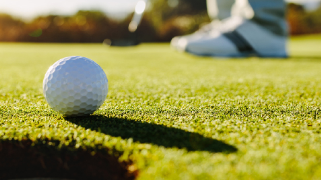 golf ball on green near hole with golfer in distance