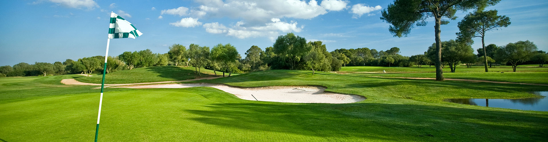 Golf green with flag and view of a bunker and water hazard.
